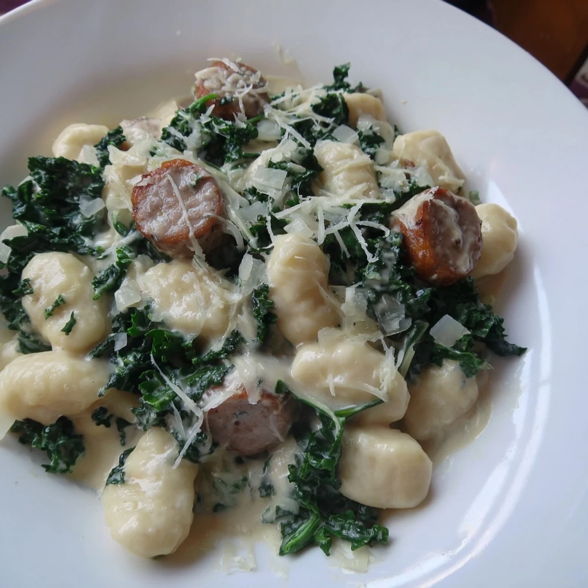 Close-up of golden-brown sausage and tender kale in the rich creamy gnocchi dish.