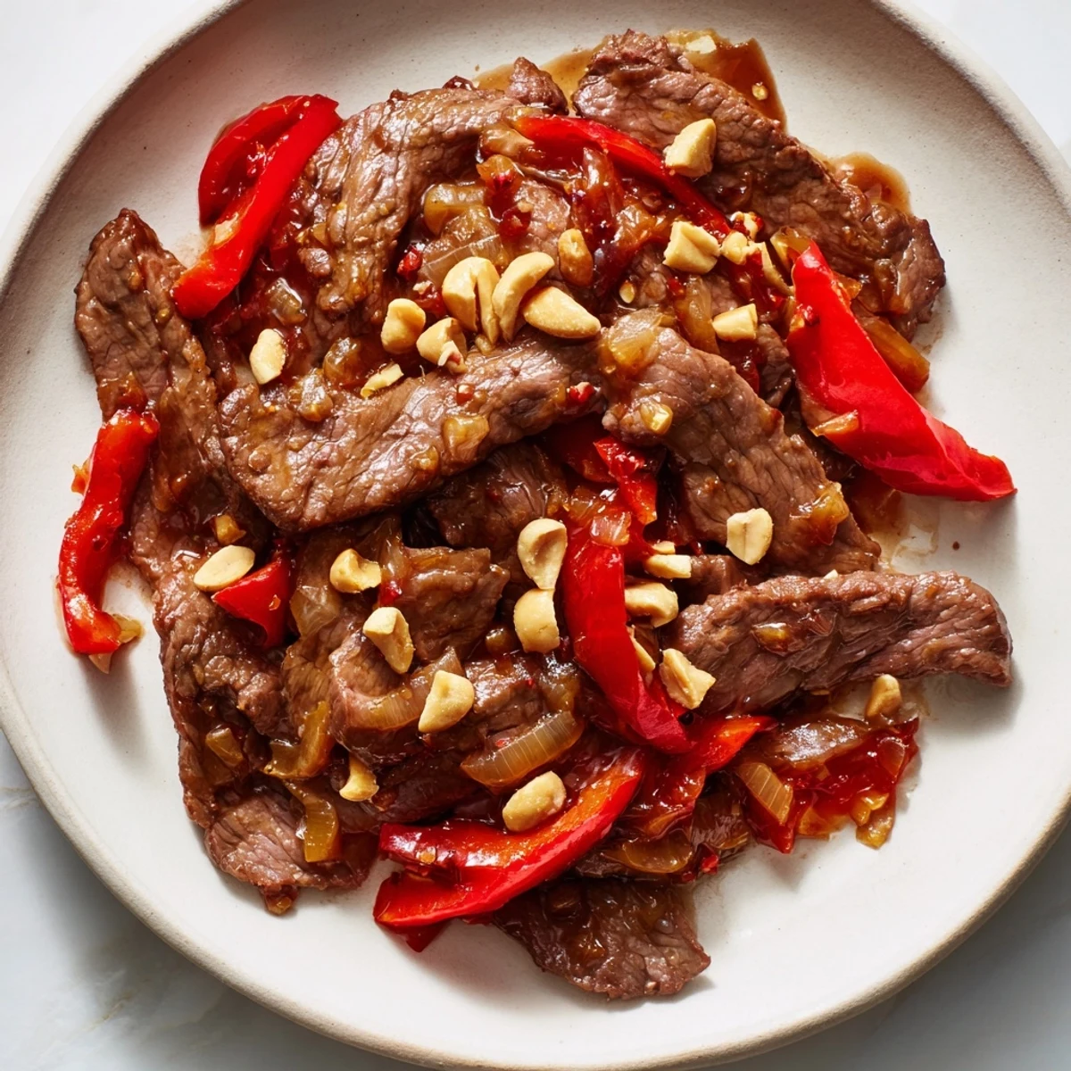 A hot wok holds Spicy Szechuan Beef with Peanuts, garnished with scallions and chili peppers.