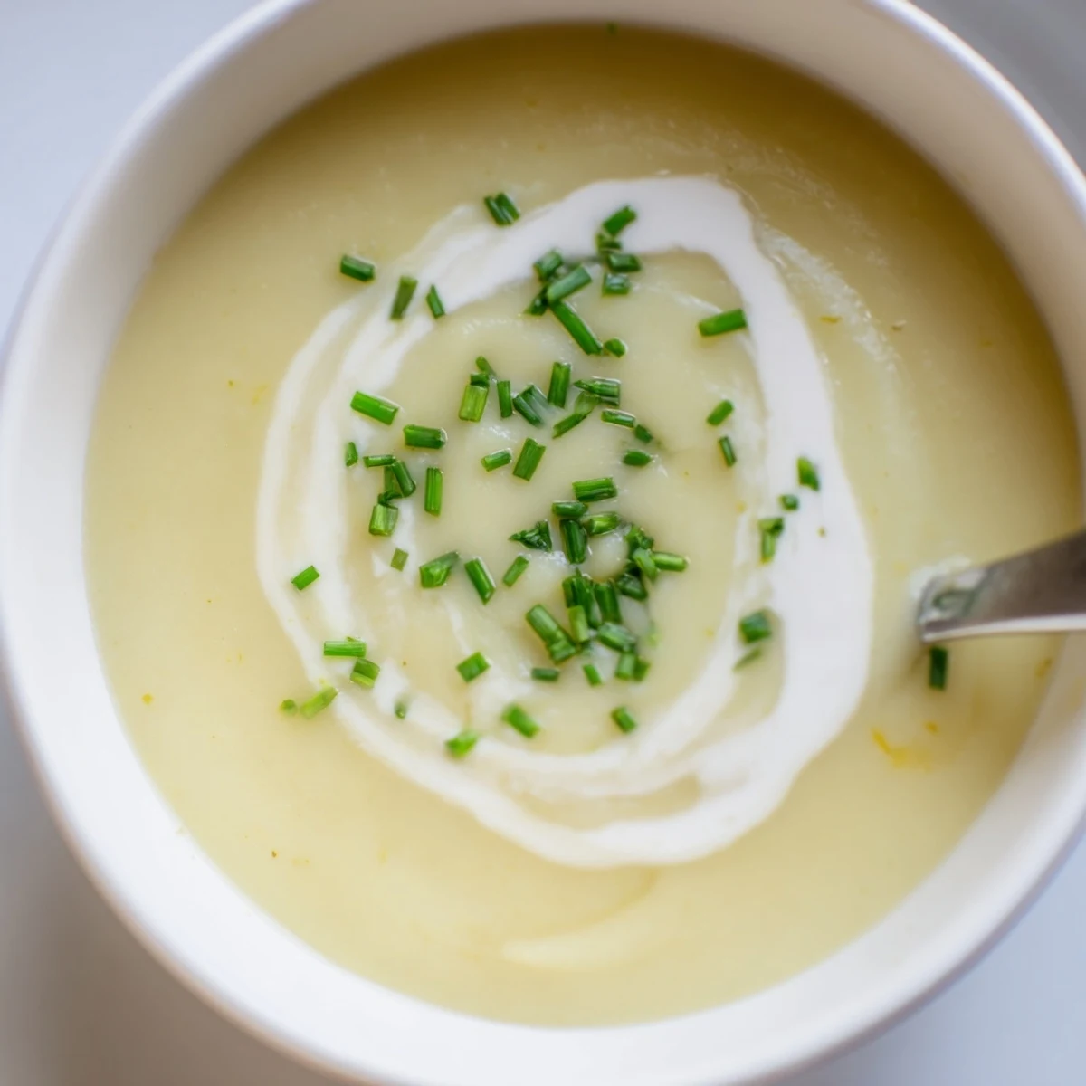 Creamy Potato Leek Soup with Chives garnished with fresh chives and a drizzle of cream in a rustic bowl.