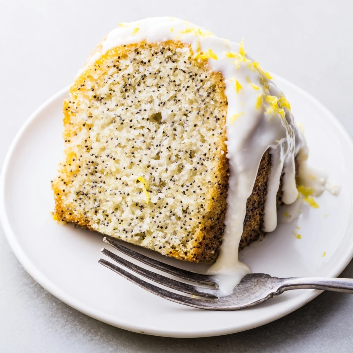 A slice of the glazed Lemon Poppy Seed Bundt Cake rests on a dessert plate, ready to serve.