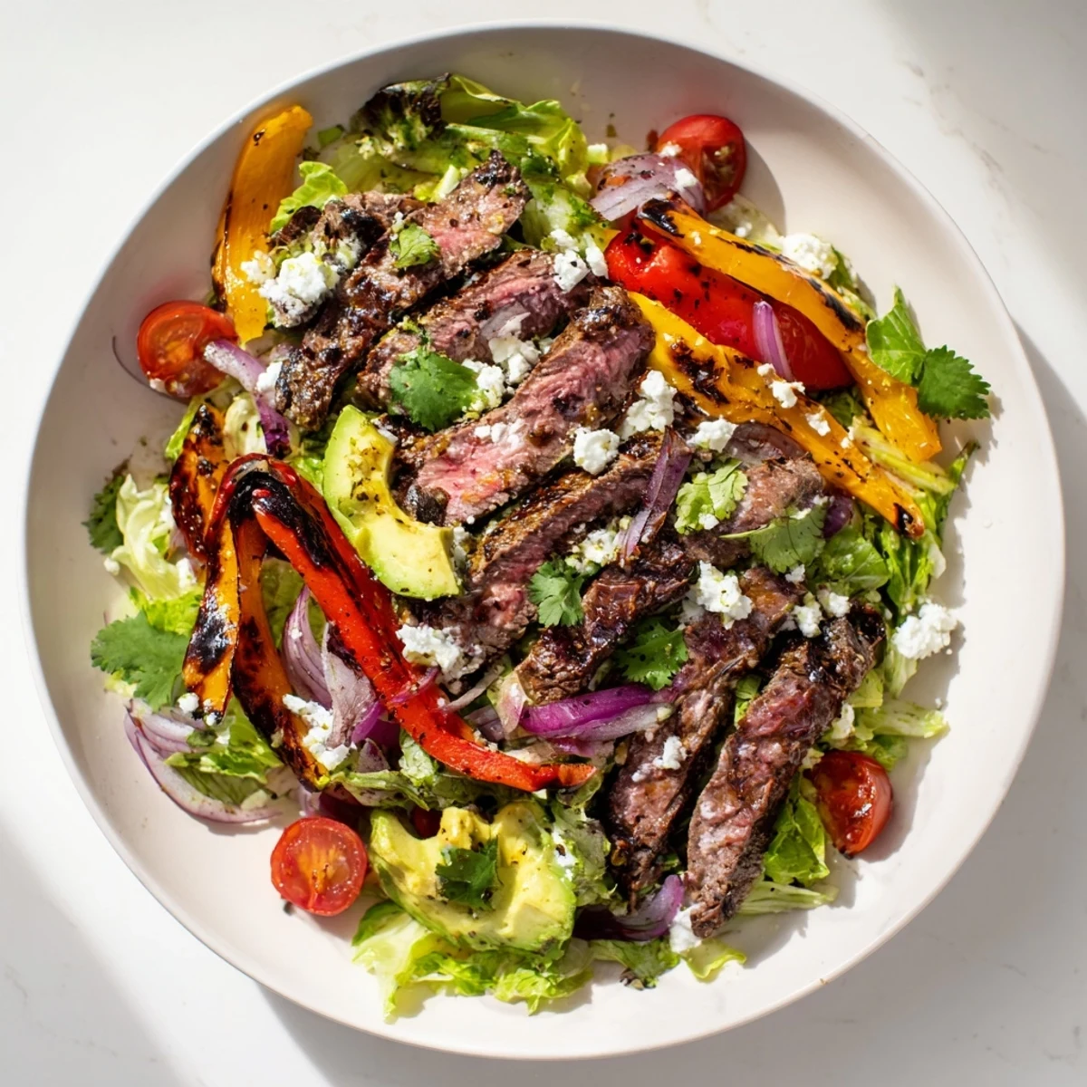 Vibrant Beef Fajita Salad with grilled flank steak, colorful peppers, onions, and creamy avocado on fresh greens, drizzled with lime vinaigrette.  
