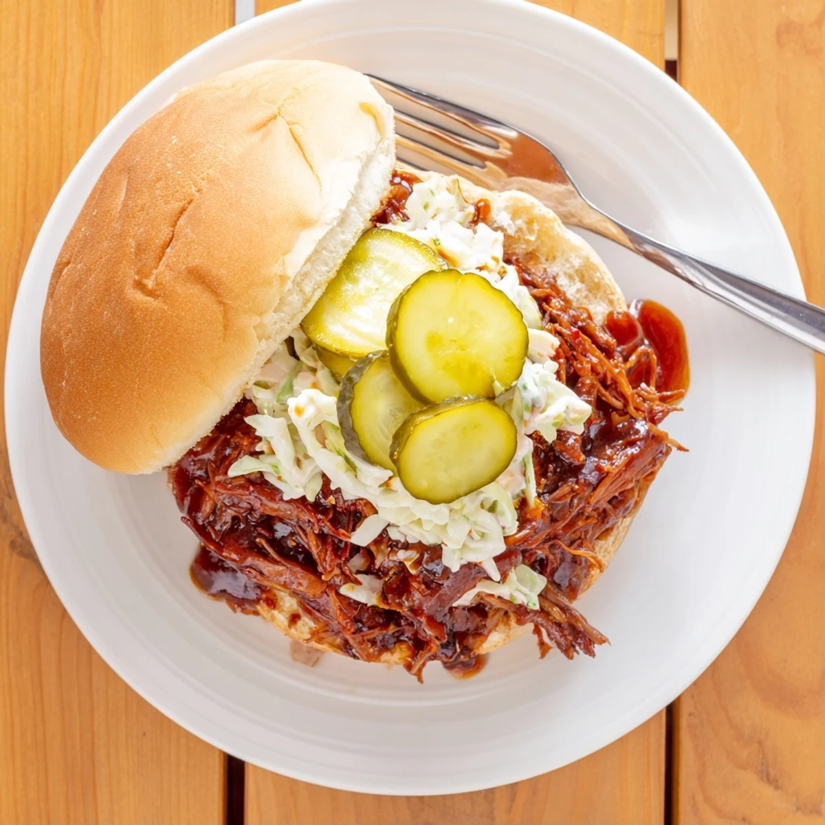 A rustic plate of Slow Cooker Pulled Beef Sandwiches with buns, extra sauce, and crisp coleslaw on a wooden table.