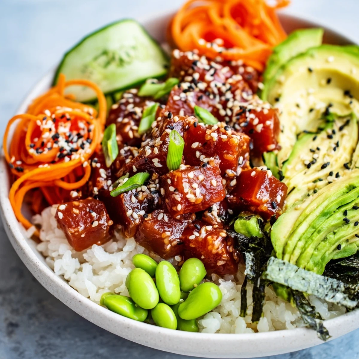 An inviting Spicy Tuna Poke Bowl topped with edamame, nori strips, and a sprinkle of sesame seeds, served on a ceramic counter.