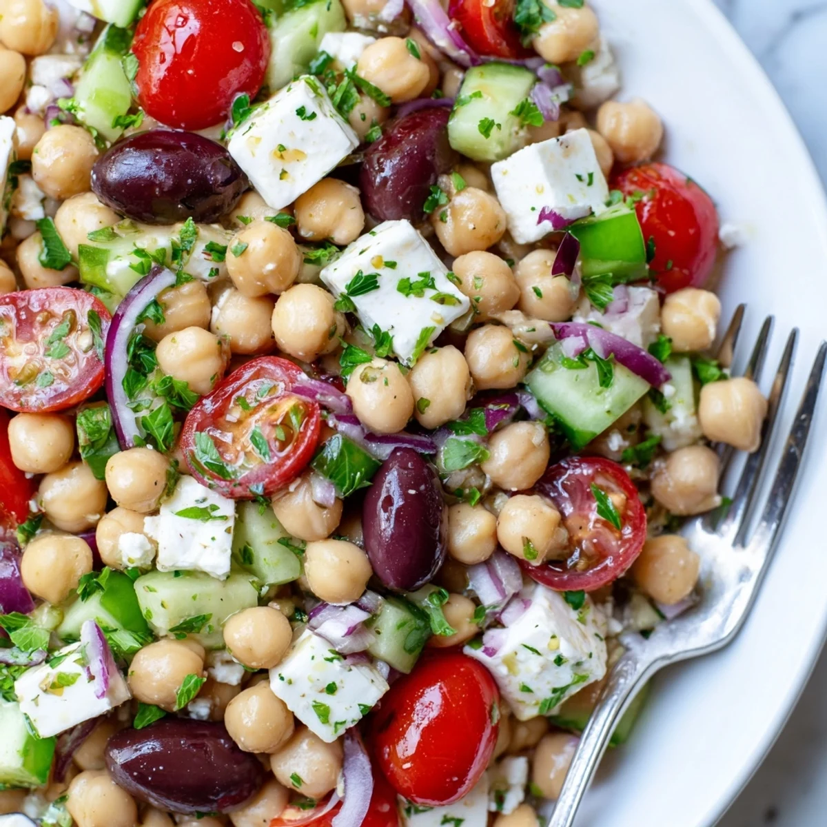Overhead view of Mediterranean Chickpea Salad with Feta, featuring vibrant red tomatoes, green cucumbers, and purple olives; ready to serve chilled on a rustic table.