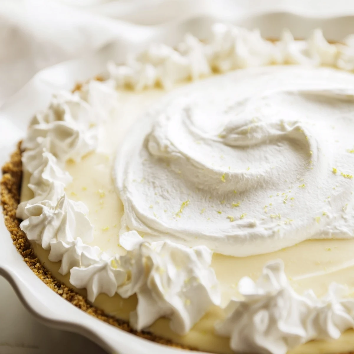 A slice of Key Lime Pie with Whipped Cream Topping reveals a creamy, pale-green filling in a golden graham cracker crust, topped with fluffy white cream and a sprinkle of lime zest.