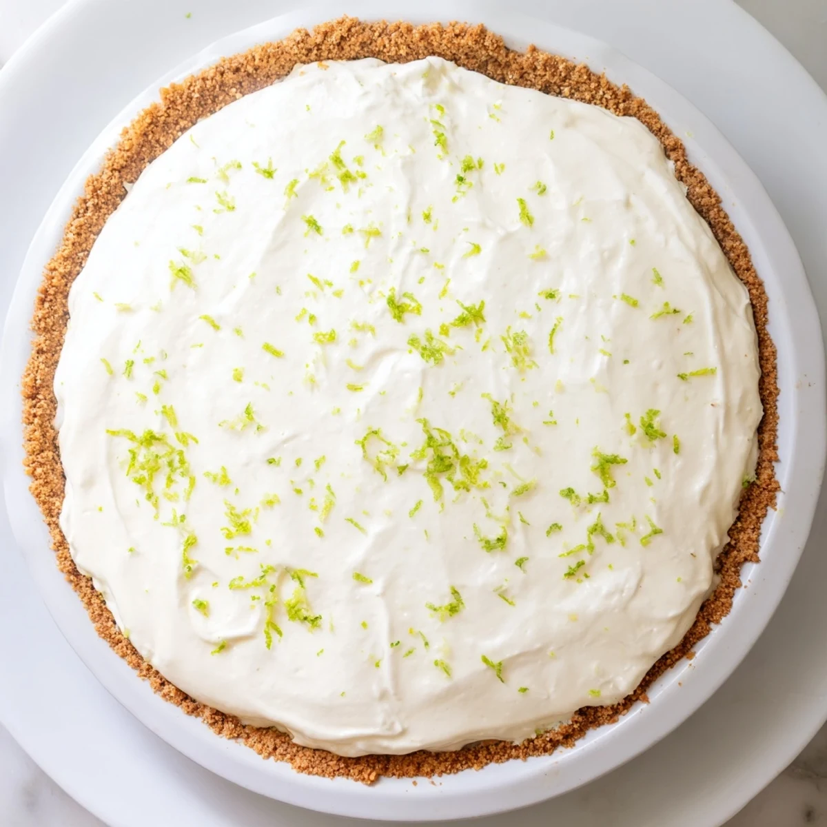 A freshly baked Key Lime Pie with Whipped Cream Topping shows a smooth, pale yellow filling in a golden graham cracker crust, topped with soft swirls of white cream and lime zest.  