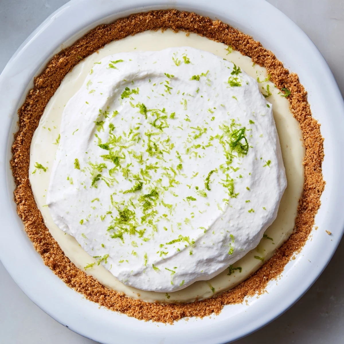 This Key Lime Pie with Whipped Cream Topping features a billowy whipped cream peak garnished with lime zest, emphasizing the refreshing citrus aroma and creamy texture.