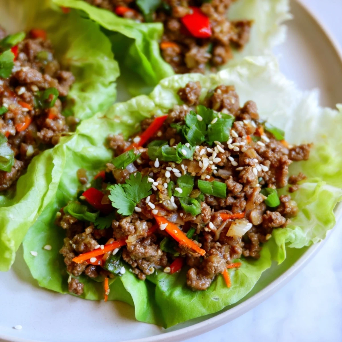 Beef Lettuce Wraps with Hoisin Sauce plated with colorful bell peppers and shredded carrots, garnished with sesame seeds.