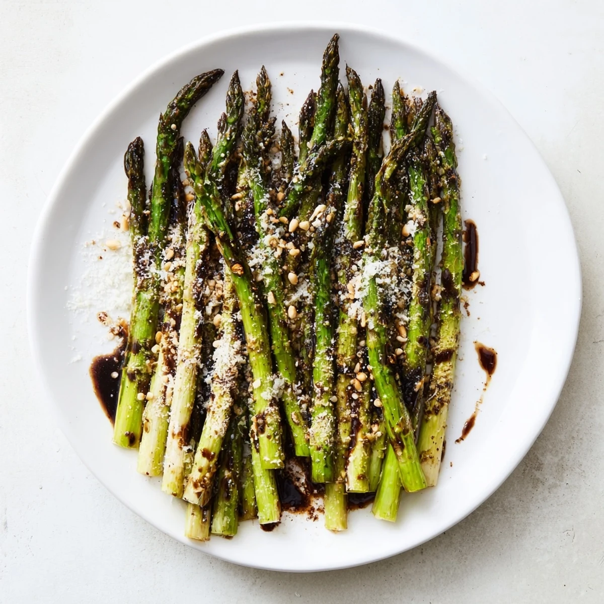 Vibrant green roasted asparagus drizzled with sweet and tangy balsamic glaze garnished with toasted pine nuts for extra crunch.