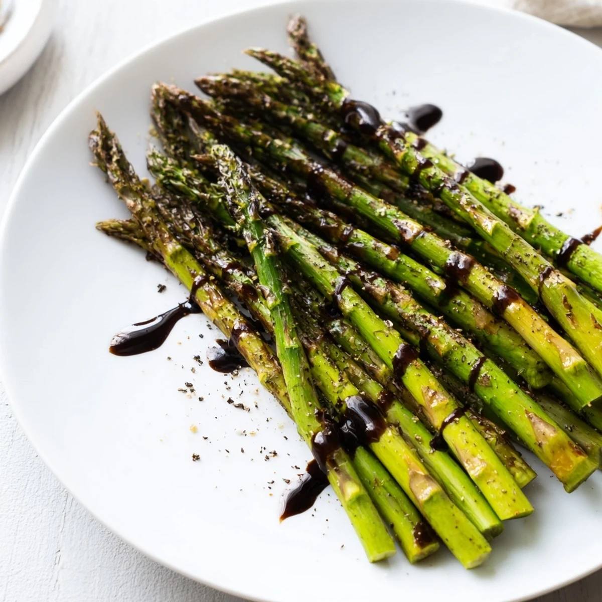Fresh asparagus roasted with olive oil and black pepper, drizzled with a thick balsamic reduction, creating an elegant vegetarian side dish for dinner.