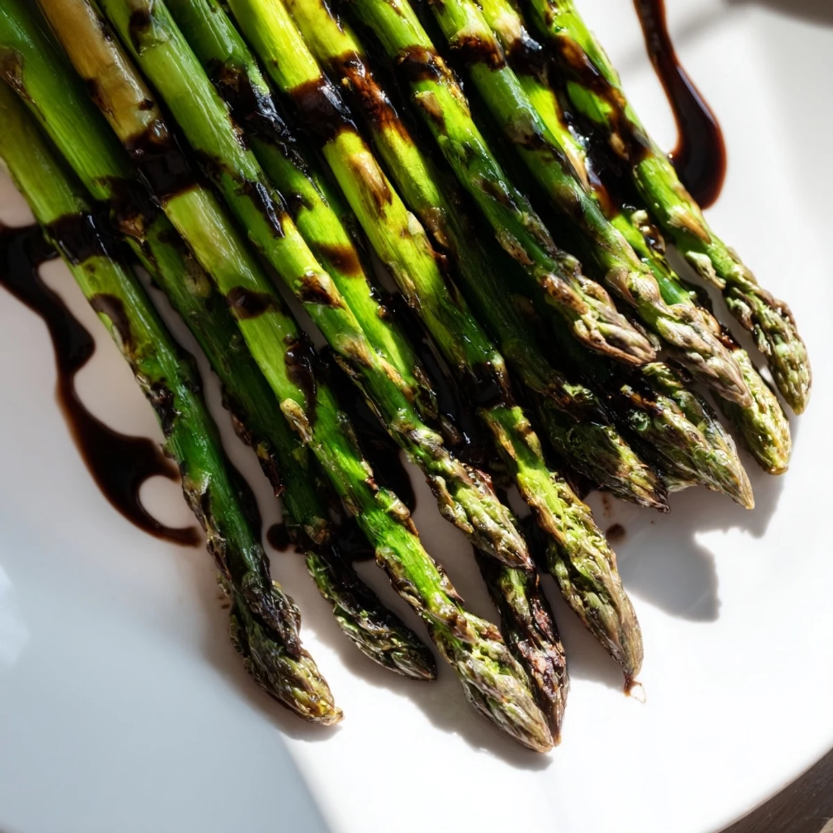 Fresh roasted asparagus with balsamic glaze garnished with pine nuts on a rustic wooden table.