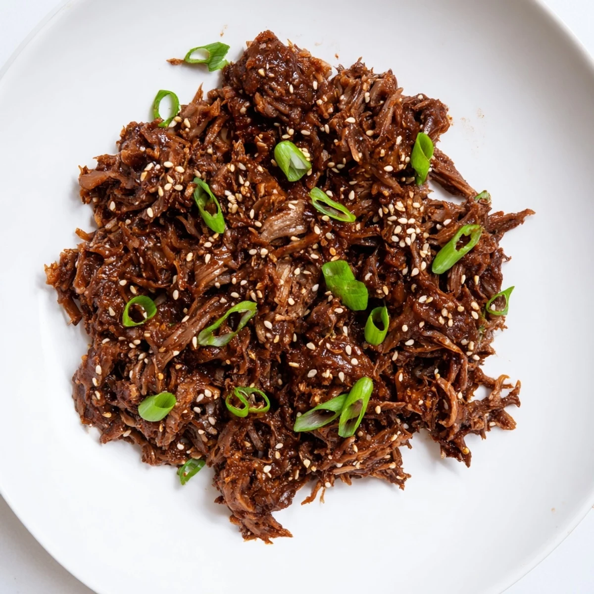 Slow cooker Korean beef simmering in a rich, reddish-brown sauce, garnished with fresh green onions and sesame seeds.