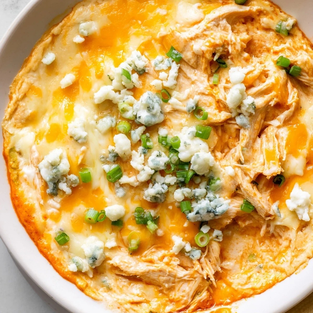 A creamy and spicy Keto Buffalo Chicken Dip in a white baking dish, topped with green onions and blue cheese crumbles for game day.