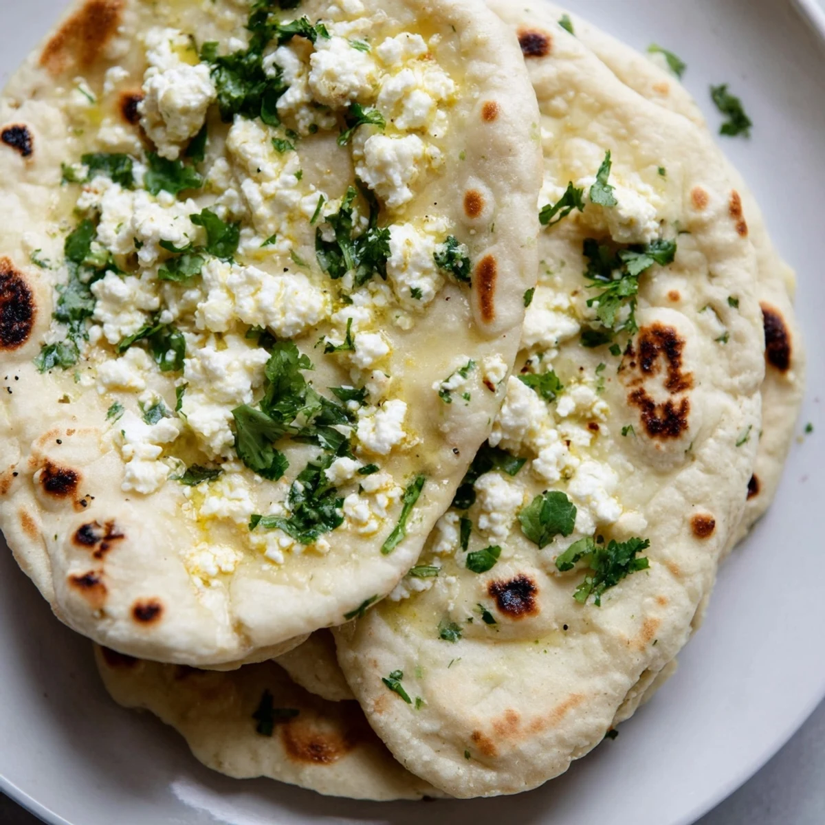Golden-brown Cottage Cheese Garlic Naan topped with fresh cilantro and garlic butter, served warm alongside a rich curry dish on a rustic plate.