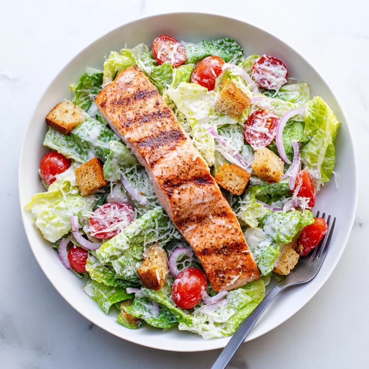 Grilled salmon fillet resting atop crisp romaine Caesar salad with homemade creamy dressing and crunchy croutons