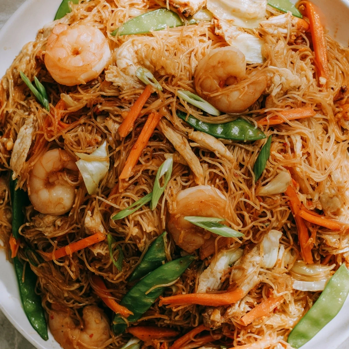 Sizzling plate of traditional Pancit Bihon stir-fry garnished with fresh scallions and lemon wedges.