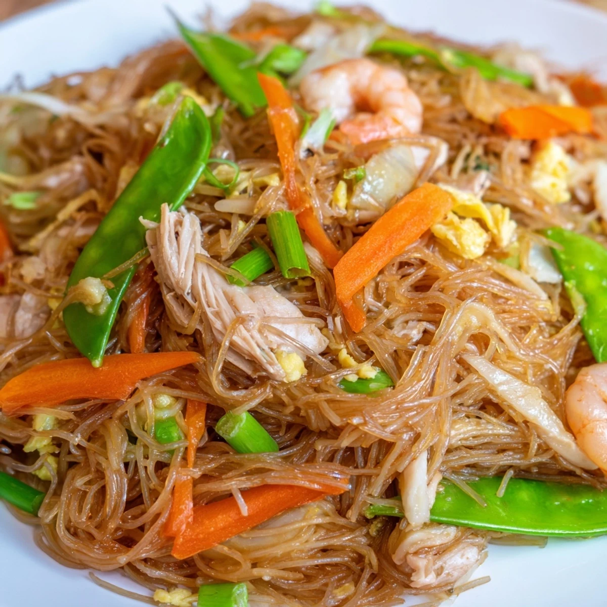 Golden Pancit Bihon noodles tossed with chicken, shrimp, and colorful vegetables in a savory soy sauce.