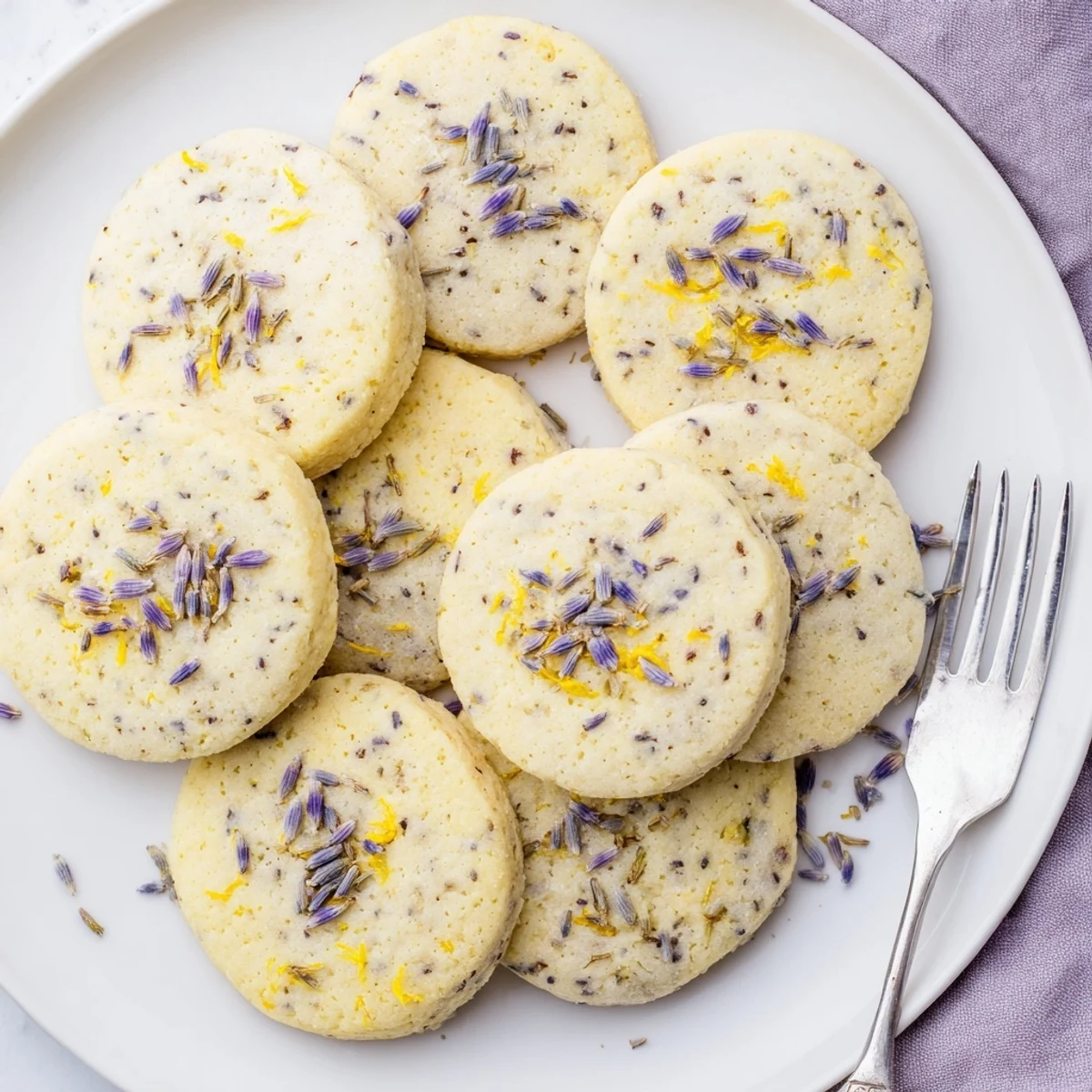 Golden lemon lavender cookies with flecks of bright zest and purple lavender buds on a white plate