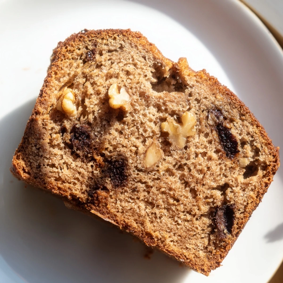 Golden moist banana bread loaf with a cracked top, sliced on a wooden cutting board