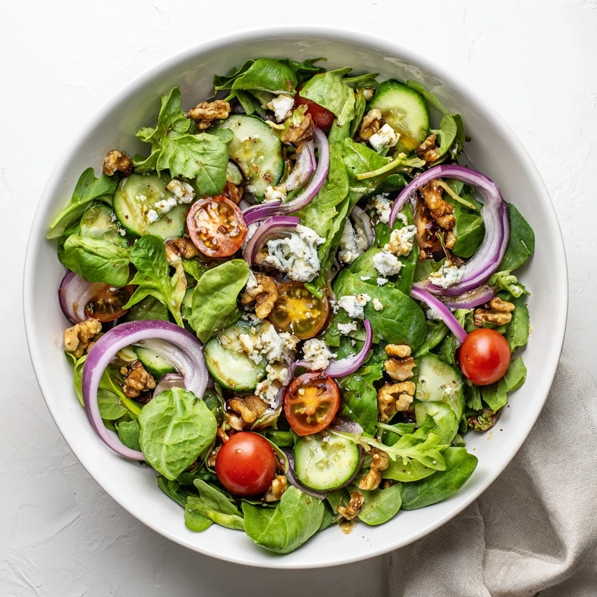 Colorful spring mix salad featuring balsamic honey dressing, red onion, and crumbled feta cheese on a white plate