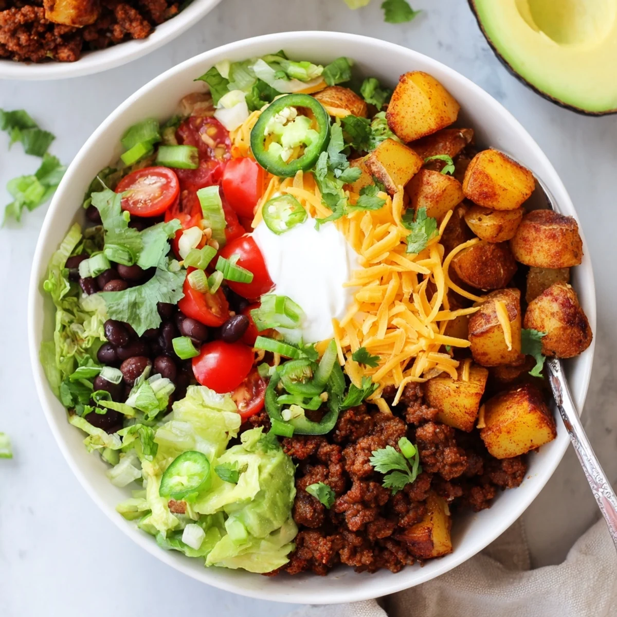 Hearty loaded potato taco bowl with golden potatoes, seasoned ground beef, cheese, sour cream, and vibrant vegetables
