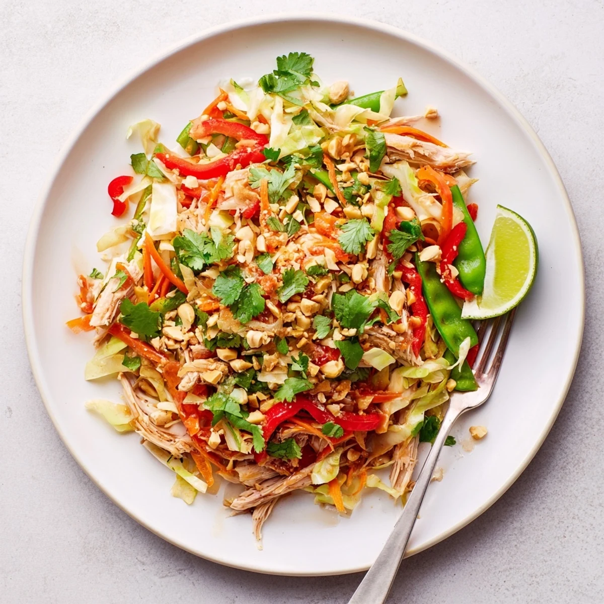 Vibrant Asian chicken salad bowl featuring shredded chicken, crisp cabbage, carrots, and crunchy peanut toppings.