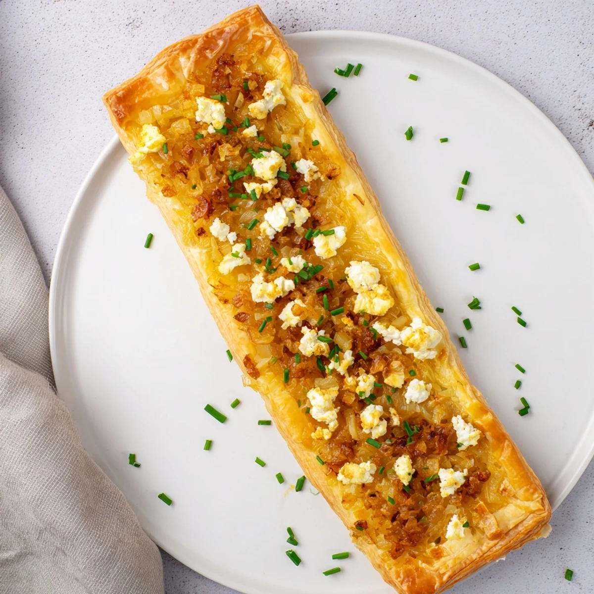 Golden brown caramelized onion and goat cheese tarts on puff pastry with fresh herbs garnish