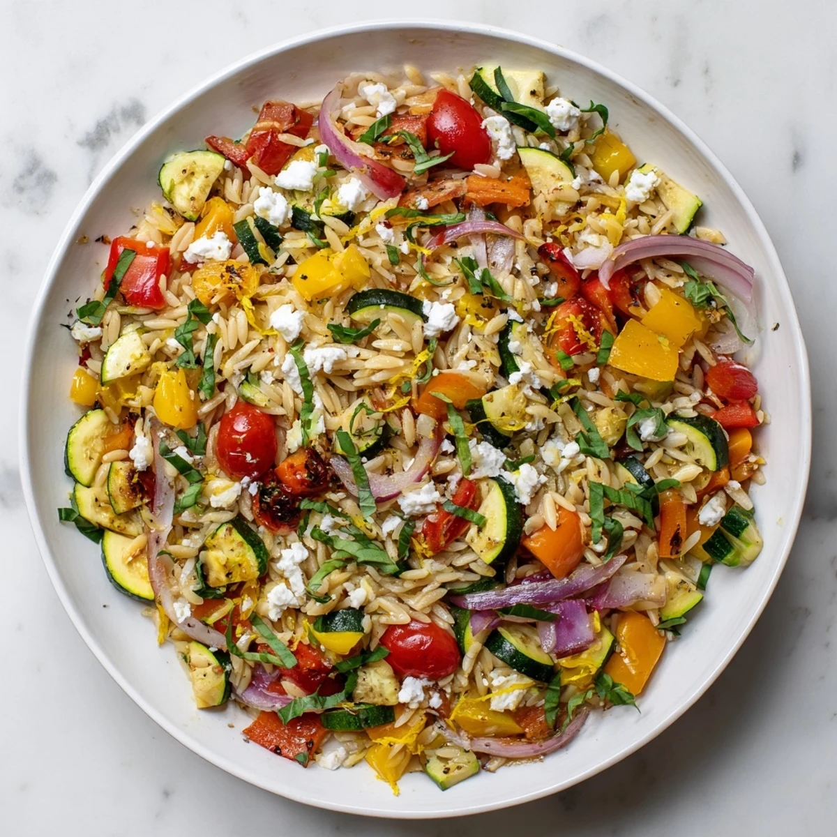 Close up of tender roasted vegetable orzo with fluffy feta cheese basil and parsley on rustic table