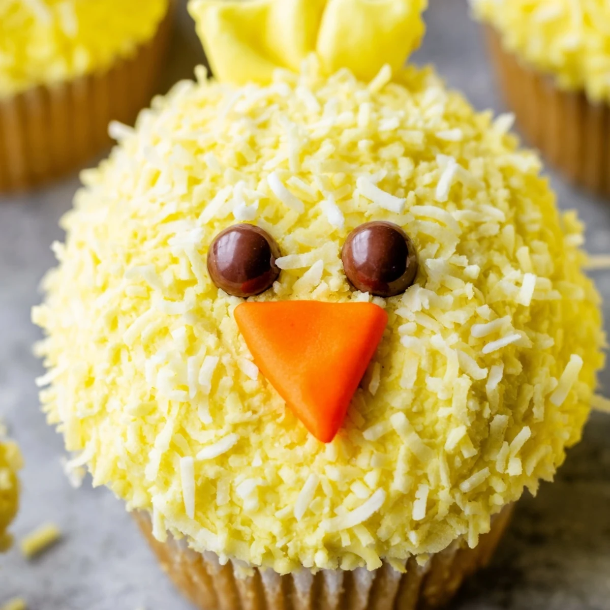 Cute Easter Chick Cupcakes decorated with bright yellow buttercream coconut feathers and orange candy beaks