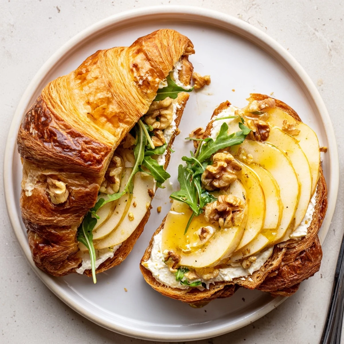 Buttery Apple Goat Cheese Croissant Sandwich layered with arugula, honey drizzle, crunchy nuts