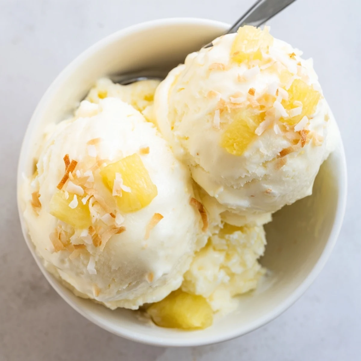 Creamy Pineapple Ice Cream topped with toasted coconut, chilled in bowl.