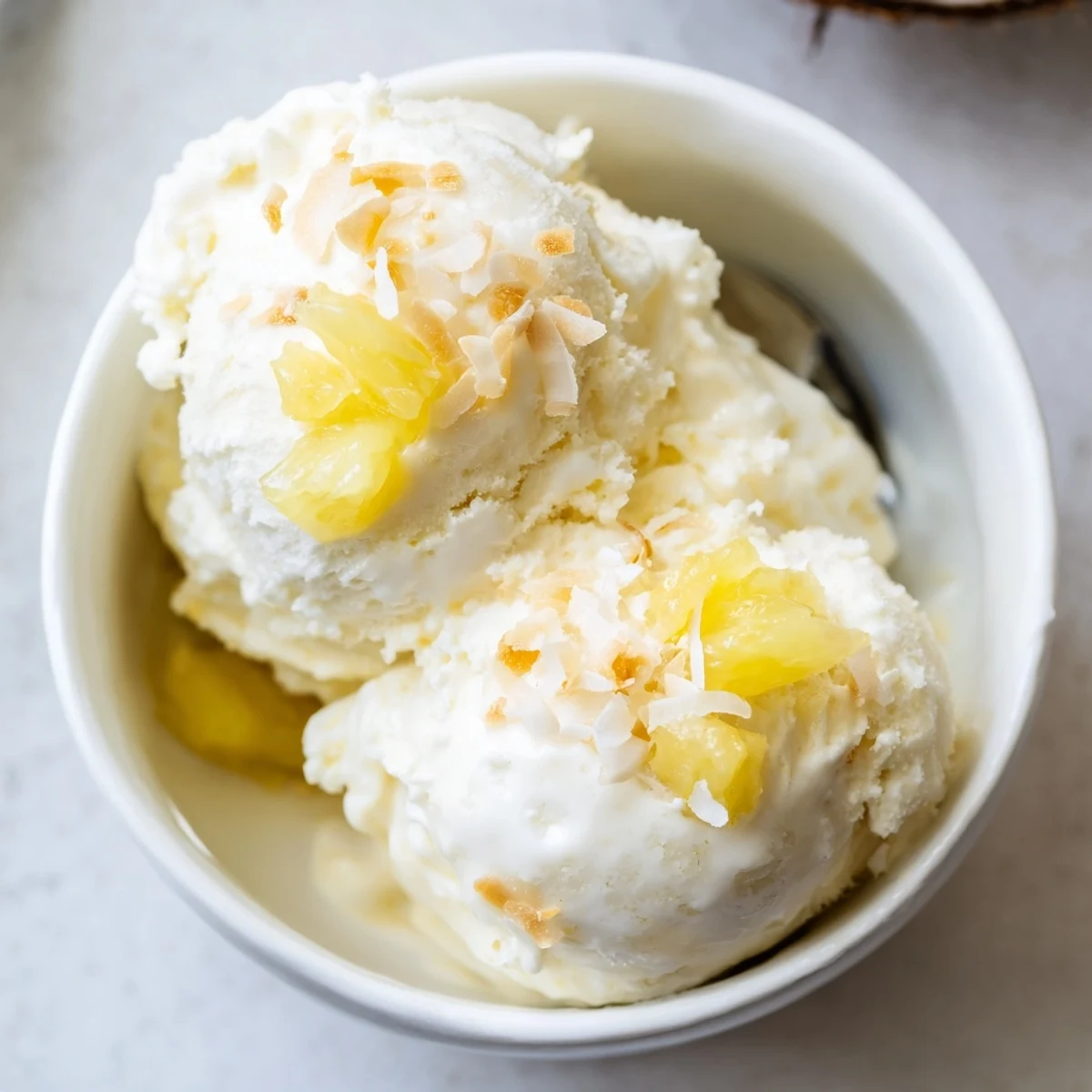 A scoop of Creamy Pineapple Ice Cream melting slightly on plate.