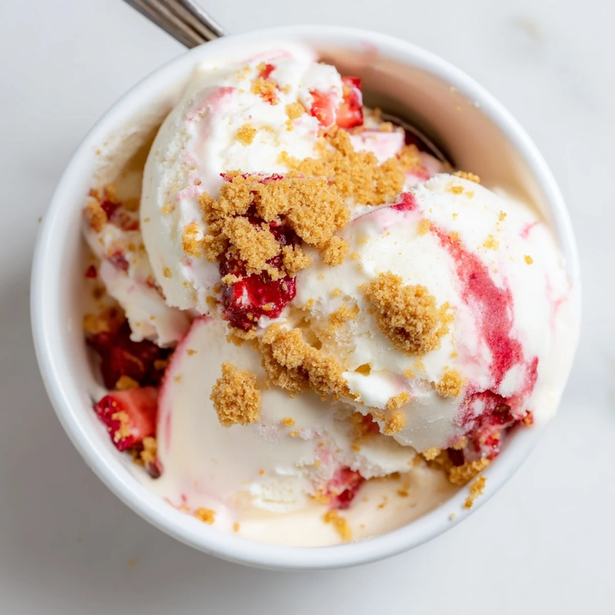 Decadent churn strawberry cheesecake ice cream featuring marbled strawberry sauce and buttery graham cracker topping
