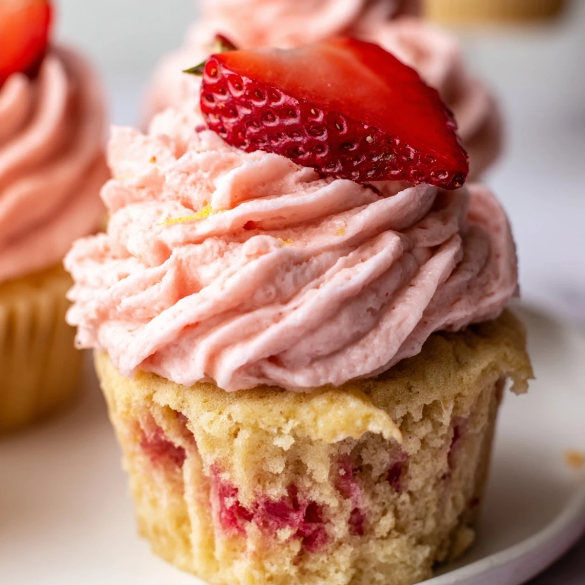 Frosted strawberry lemonade cupcakes topped with creamy pink buttercream and fresh strawberry garnish