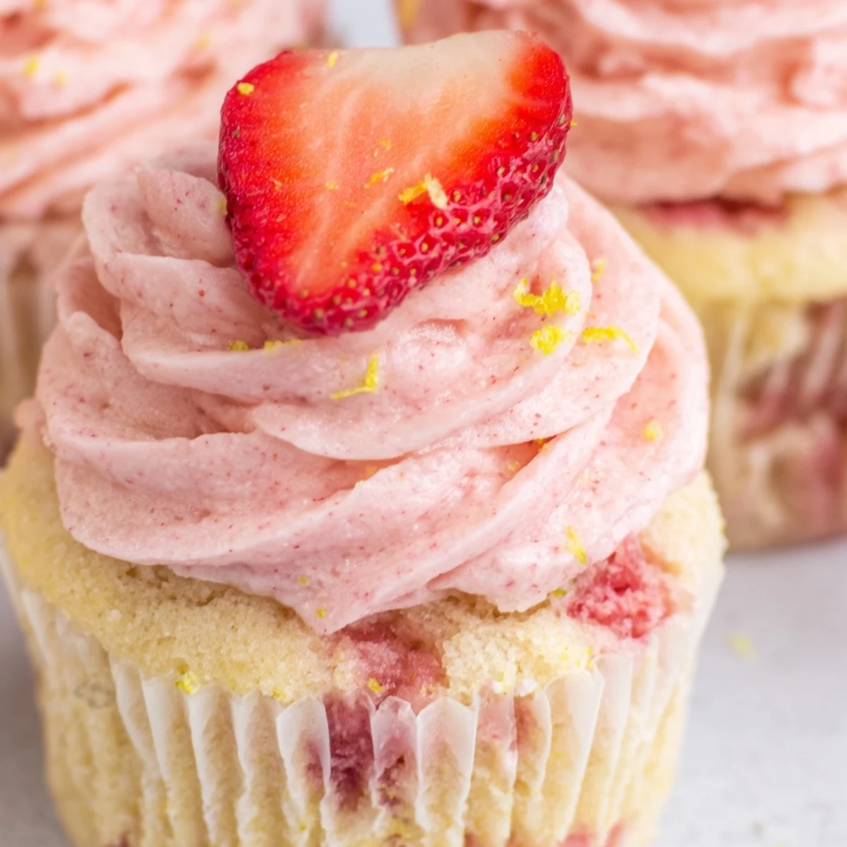 Fresh strawberry lemonade cupcakes on a white plate topped with pale pink strawberry buttercream icing