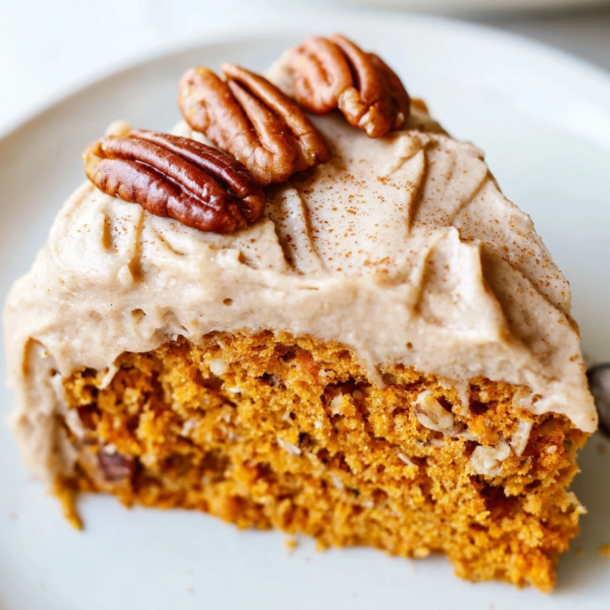 A frosted pumpkin pecan cake garnished with toasted pecan halves and a dusting of cinnamon