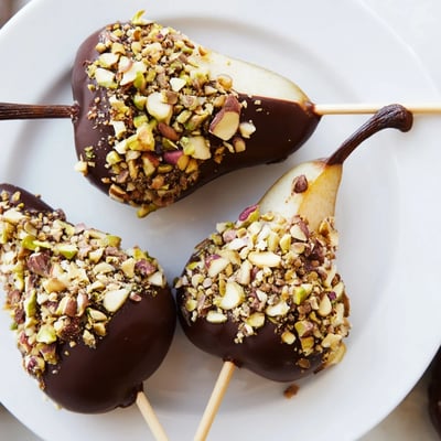 Ripe pears dipped in glossy chocolate and topped with chopped pistachios and almonds, perfect for a party platter.