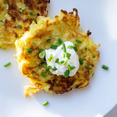 Crispy, pan-fried potato cakes flecked with green scallions, ready to be enjoyed with tangy sour cream and fresh chives.  