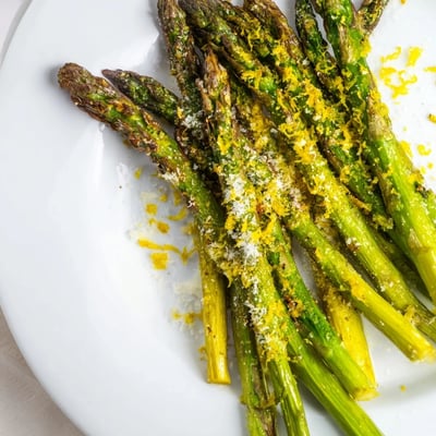 Golden roasted asparagus with parmesan and lemon, drizzled with olive oil and arranged on a baking sheet.
